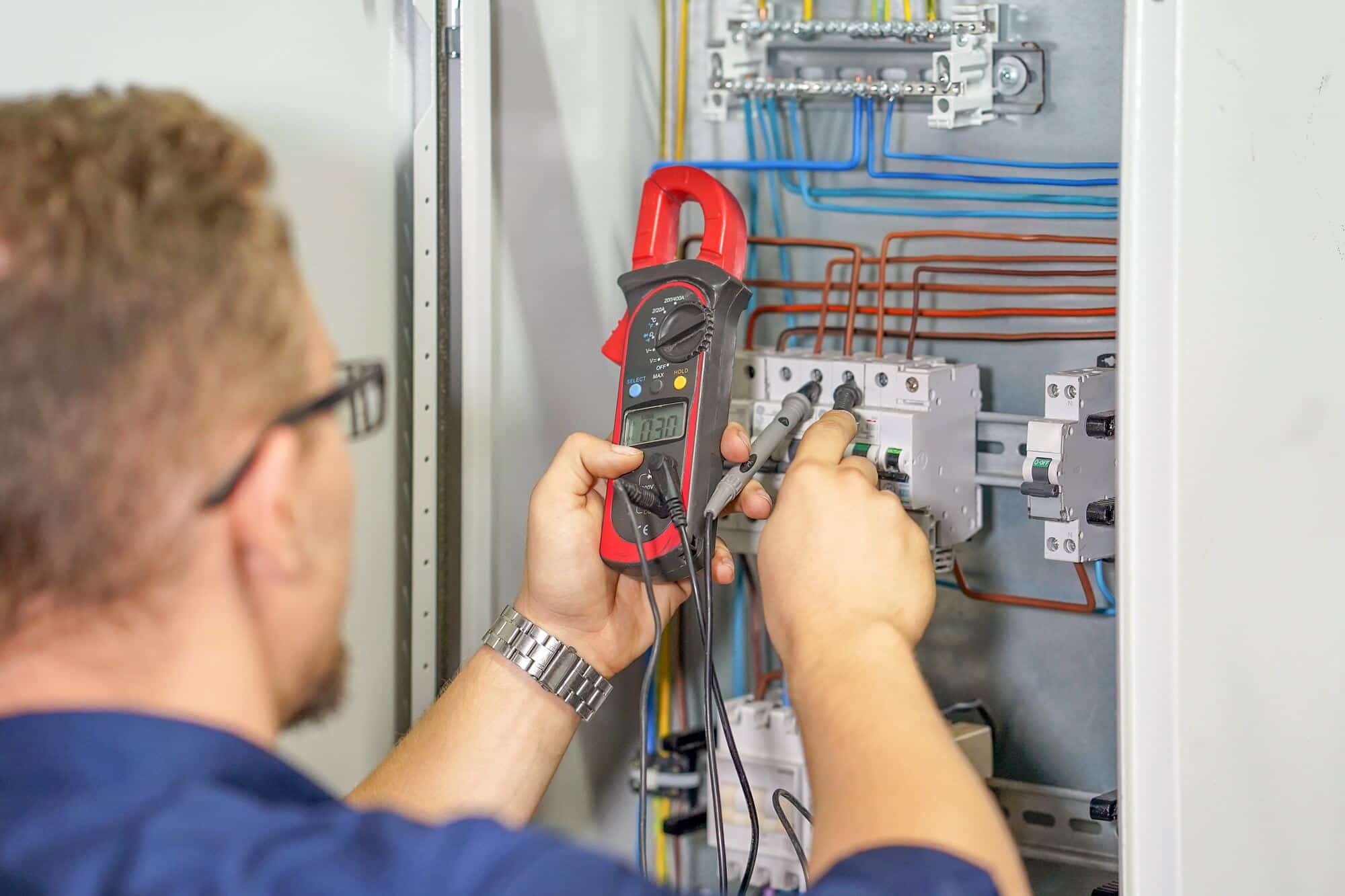 Elektriker mäter med tångamperemeter i en elcentral